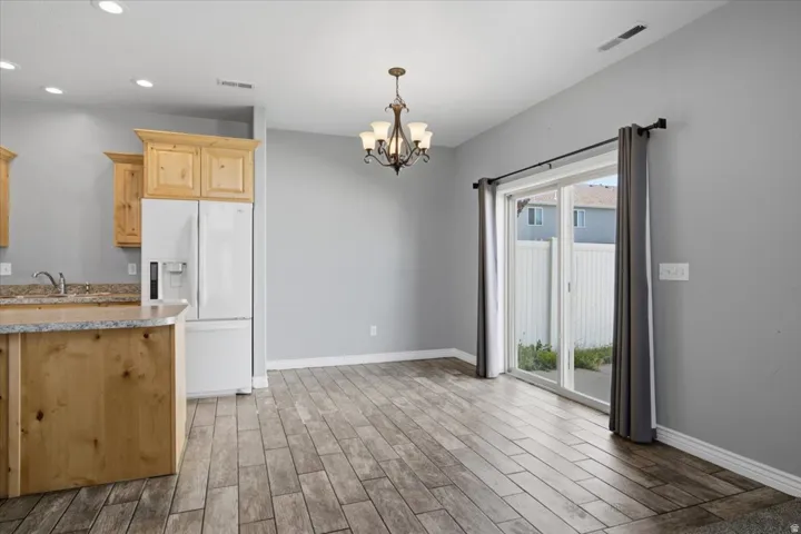 Wood-finish plank flooring, light wood cabinetry, white refrigerator, and a sliding glass door