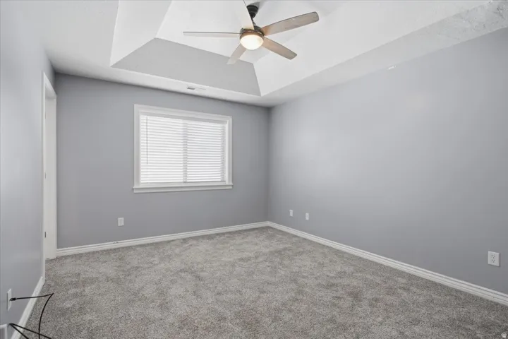 Tray ceiling with a ceiling fan, light gray wall paint, white trim, and gray carpeting
