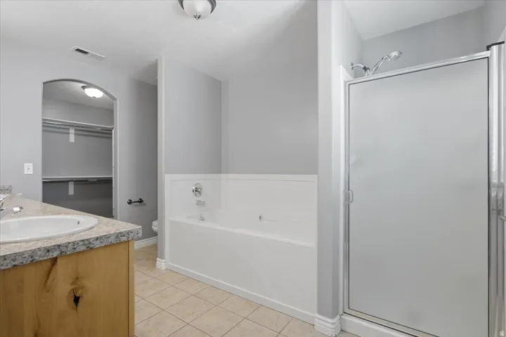 Tile flooring, wood-finish vanity with an integrated sink, stone-finish countertop, built-in bathtub, and a glass-enclosed shower