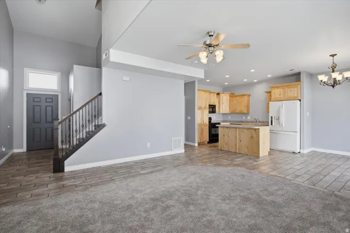 Open-concept living space with wood-finish flooring, a kitchen featuring light wood cabinetry and an island, a dark wood staircase with wrought iron balusters, and a ceiling fan
