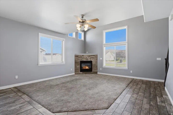 Vaulted ceiling with a ceiling fan, corner fireplace with a stone surround, and large windows