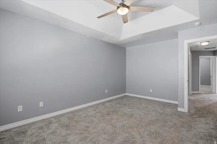 Tray ceiling with a ceiling fan, light gray wall paint, gray carpet flooring, and white trim