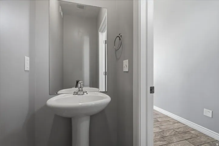 Pedestal sink with chrome faucet, wall-mounted mirror, and tile flooring