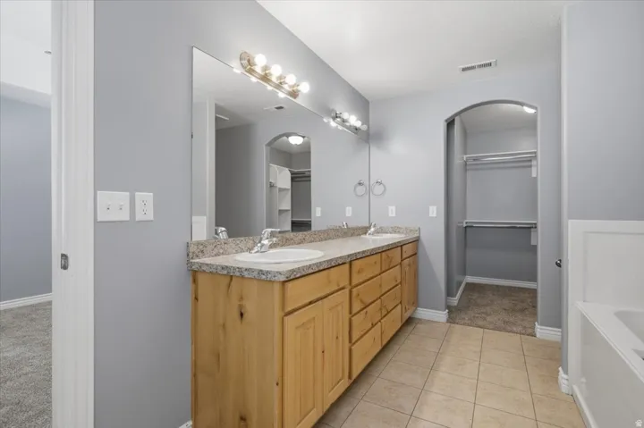 Dual vanity with wood-finish cabinetry, granite-style countertop, and ceramic tile flooring