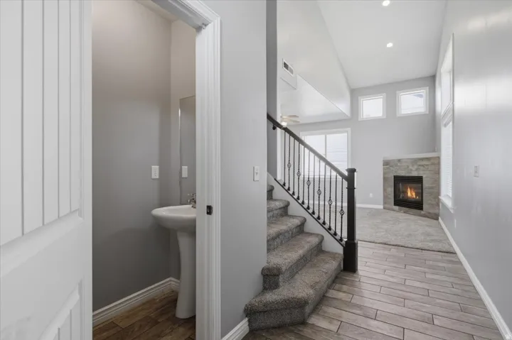 Pedestal sink with mirror, wood-finish flooring, carpeted staircase with wrought iron railing, and a fireplace with a stone surround