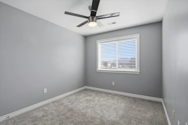 Neutral-toned walls, ceiling fan, white window trim, horizontal blinds, and grey carpeting