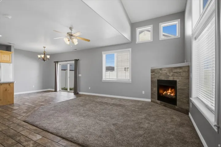 Vaulted ceiling with a ceiling fan, stone-clad fireplace, tile flooring, sliding glass door, and multiple windows