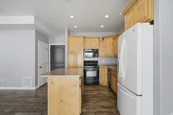 Kitchen featuring wood-finish cabinetry, black appliances, a white refrigerator, a kitchen island with a stone-finish countertop, and recessed lighting
