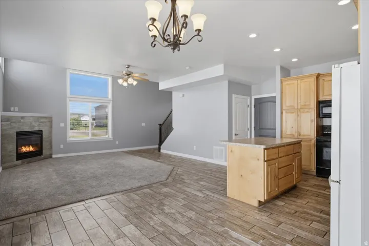 Expansive living area featuring a stone-faced fireplace, large picture windows, wood-finish flooring, and a kitchen island with built-in cabinetry
