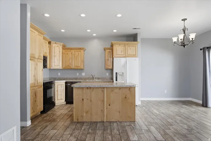 Kitchen featuring light wood cabinetry, a central island, granite-style countertops, and wood-finish flooring