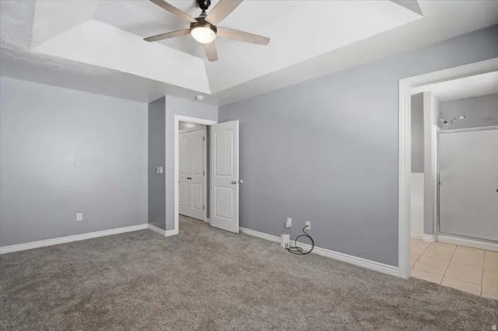 Tray ceiling with a ceiling fan, plush carpet flooring, and a shower with a glass enclosure