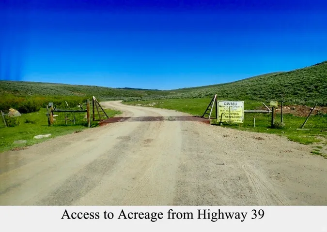 Gated property access with a gravel drive, expansive open terrain, and a naturally vegetated landscape