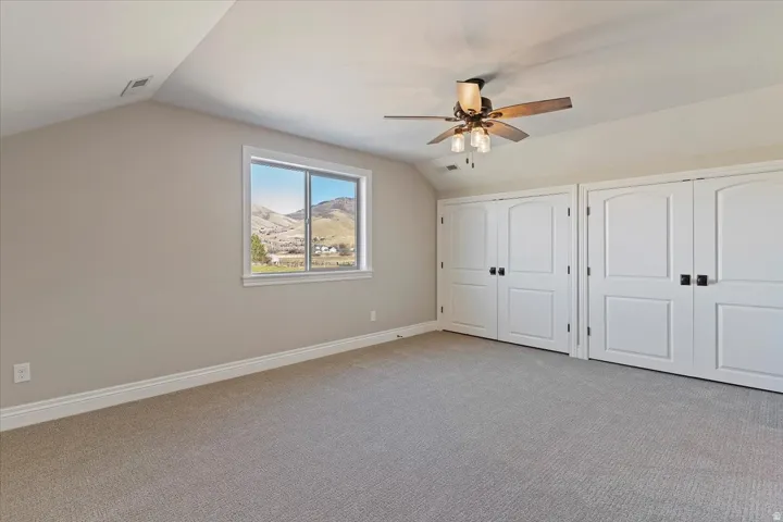 Vaulted ceiling room featuring a ceiling fan with light, a window, and two sets of double-door closets