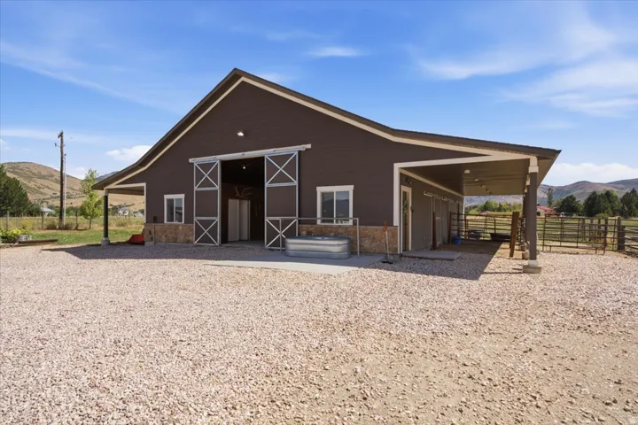 Barn structure featuring brown siding, stone wainscoting, sliding barn doors, an extended covered porch, and exterior lighting