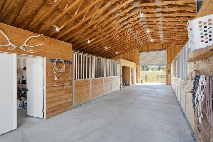 Exposed wood beam ceiling, concrete flooring, interior wood paneling, multiple partitioned stalls, and a large roll-up door