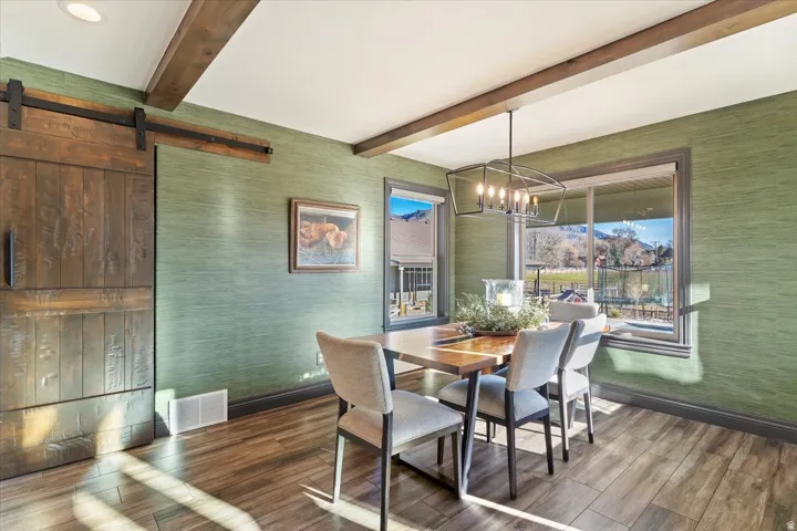 Wood-finish flooring, exposed ceiling beams, a decorative chandelier, and a barn door feature in this space