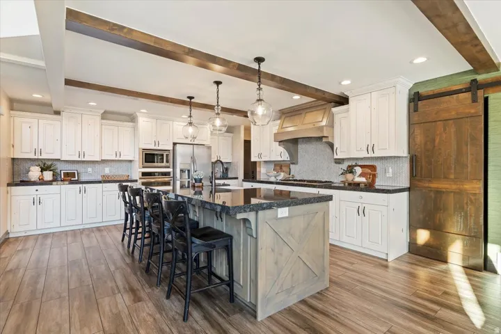 Gourmet kitchen featuring wood-finish flooring, white cabinetry, dark stone countertops, a large island with seating, and stainless steel appliances