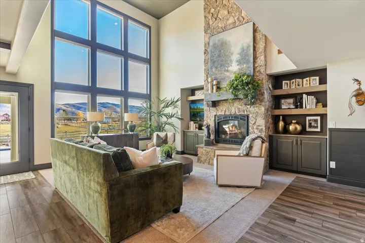 Two-story windows, stone fireplace with hearth, built-in shelving, built-in cabinetry, and wood-finish flooring
