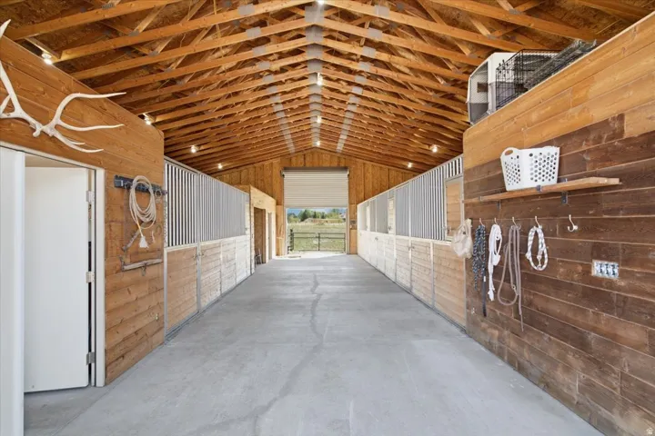 Exposed wood beam ceiling, concrete flooring, wood paneling, multiple stalls with vertical bar tops, and a roll-up door