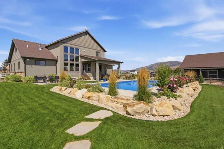 Expansive backyard featuring a manicured lawn, stone pathway, in-ground swimming pool, and established landscaping with natural rock accents