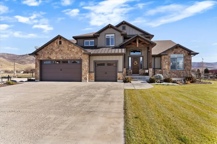 Stone and siding exterior with a multi-car garage, concrete driveway, covered entry porch with timber accents, and a landscaped front yard
