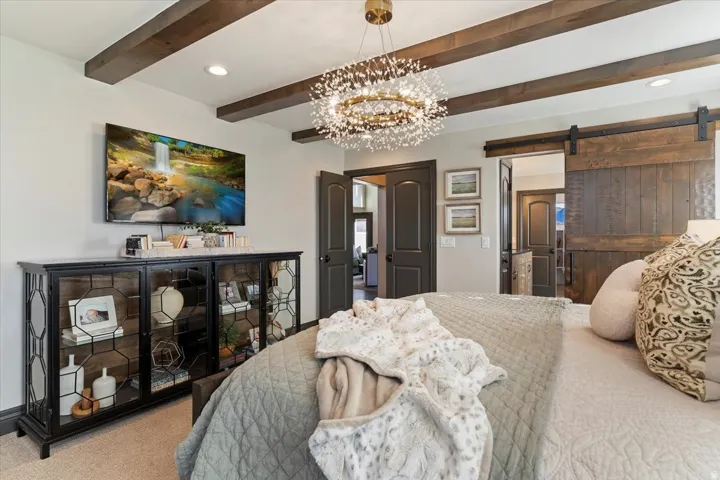 Exposed wood ceiling beams, a decorative chandelier, recessed lighting, dark interior doors, and a wood-finish barn door