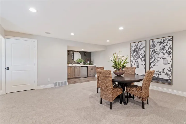 Recessed lighting, light gray carpeting, and a built-in wet bar with wood-finish cabinetry and a stainless steel under-counter refrigerator