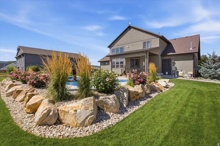 Expansive lawn area with a rock-lined garden bed, featuring mature shrubs, ornamental grasses, and blooming flowers