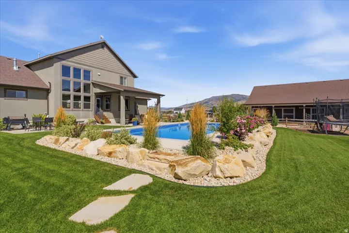 Expansive backyard featuring a manicured lawn, a built-in swimming pool, a rock garden with varied plantings, and a covered patio