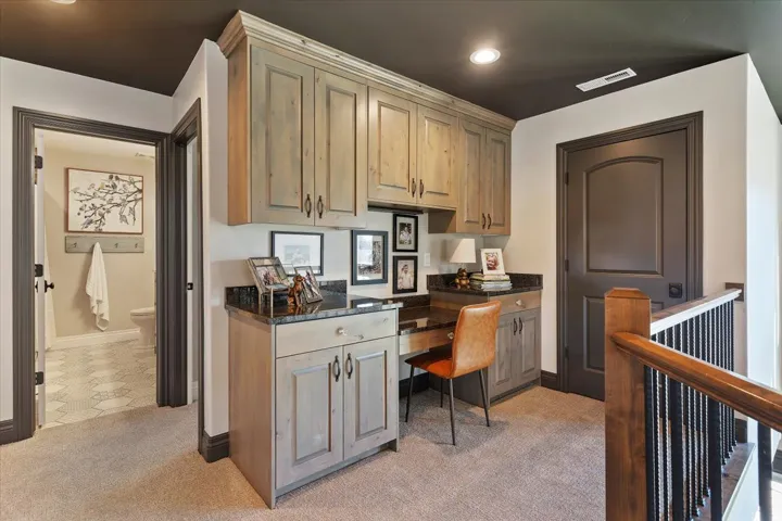 Built-in wood-finish cabinetry, black stone countertop, recessed lighting, carpet flooring, and dark wood doors