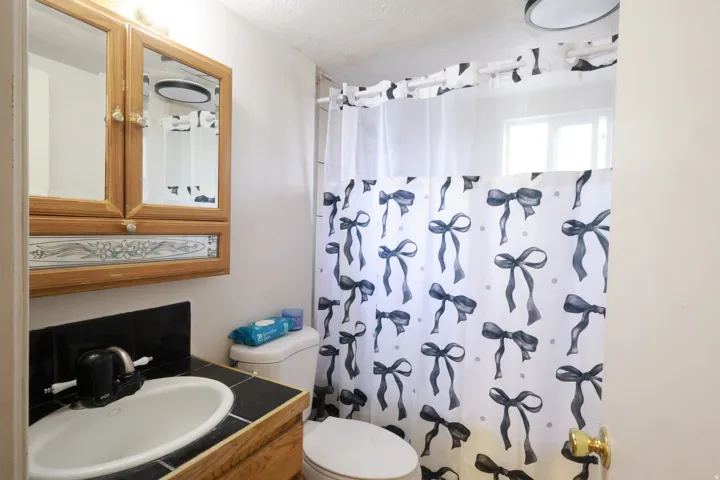 Vanity with an integrated sink and black tiled countertop, a built-in medicine cabinet with a wood-finish frame, and a window