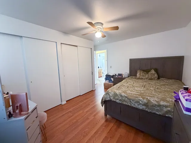 Hardwood-finish flooring, white walls, ceiling fan with integrated lighting, and multiple sliding closet doors