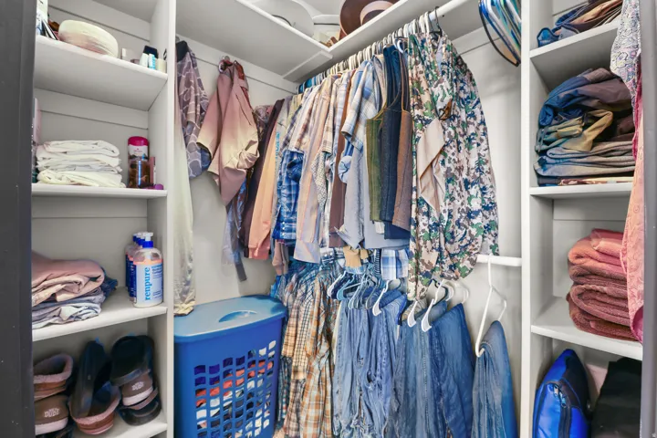 Corner closet featuring built-in shelving, multiple hanging rods, and white finishes