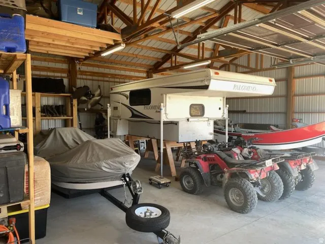 Spacious storage building featuring a metal roof, exposed wood trusses, fluorescent lighting, and a concrete floor