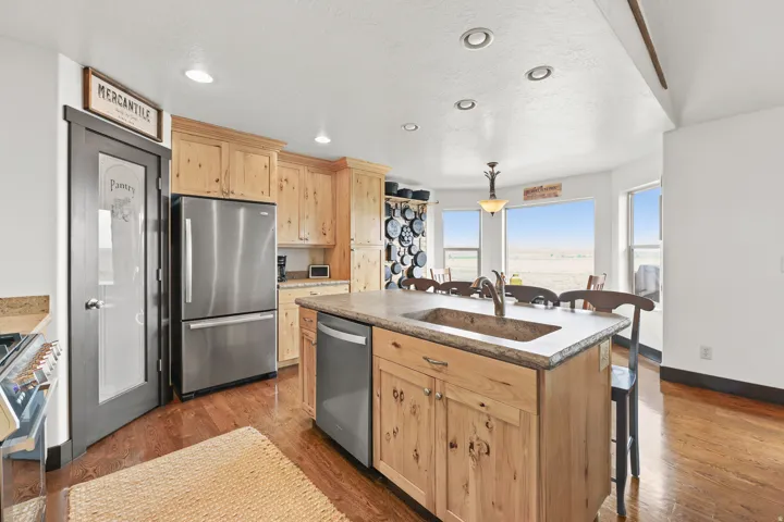 Kitchen featuring light wood cabinetry, stainless steel appliances, a center island with an integrated sink, stone countertops, and recessed lighting