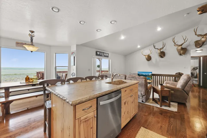 Open-concept living space featuring wood-finish flooring, a kitchen island with integrated sink, stainless steel dishwasher, and a vaulted ceiling with recessed lighting