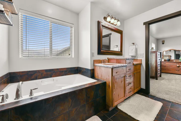 Soaking tub with tile surround, dual wood-finish vanity with countertop, wood-framed mirror, and attached light fixture