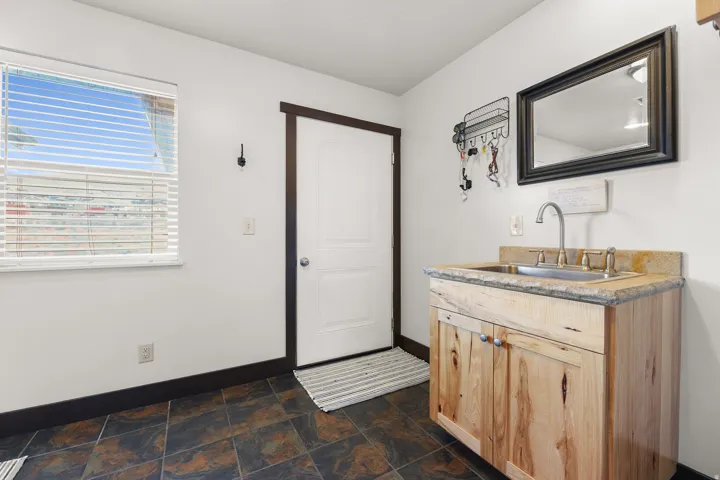 Wood-finish vanity with an integrated sink and stone-look countertop, tile flooring, and a window with blinds