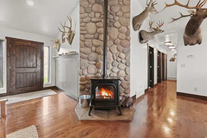Stone-clad wood-burning stove with a hearth, rich wood-finish flooring, a solid wood entry door, and recessed ceiling lighting