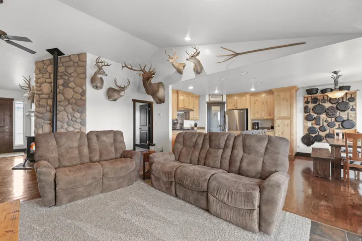 Vaulted ceilings, a stone-clad fireplace with a wood-burning stove, wood-finish flooring, a kitchen with light wood cabinetry, and stainless steel appliances