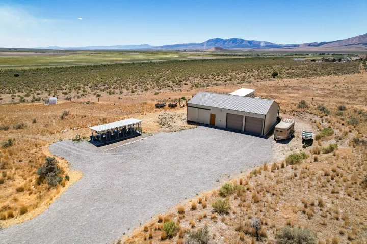 Metal-sided building with multiple roll-up garage doors, gravel driveway, and surrounding open land