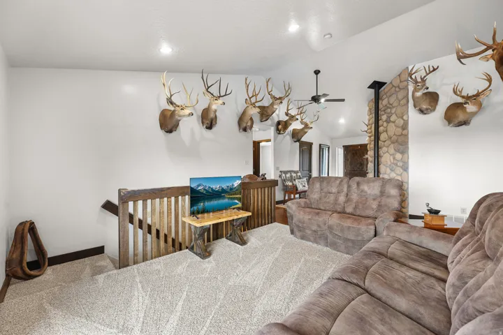 Vaulted ceilings, recessed lighting, stone-clad accent wall, ceiling fan, and wood-finish stair railing