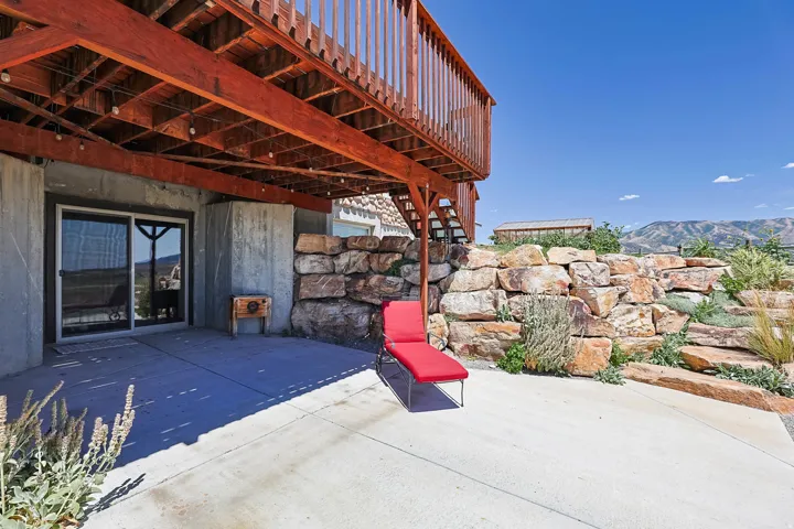 Concrete patio with a rock retaining wall, featuring a sliding glass door and a wooden deck overhead