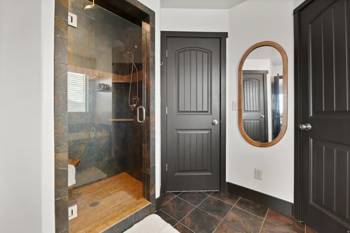 Glass-enclosed shower with stone tile surround, built-in wooden bench, and rain showerhead