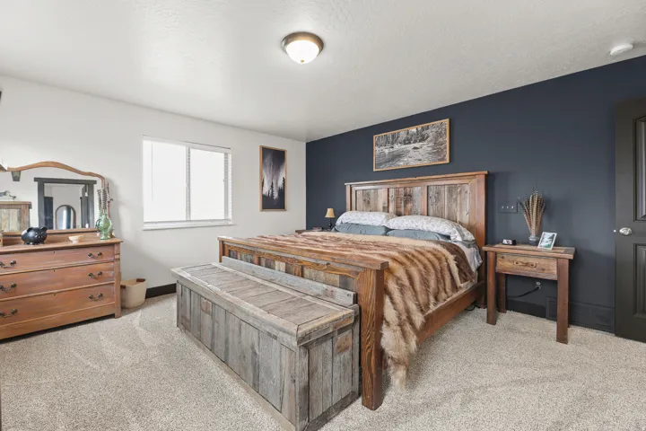 Primary Bedroom with Hardwood Bed Frame, Wood-Finish Dresser, and NightstandSpacious primary bedroom featuring rich wood furnishings, neutral carpeting throughout, and a striking navy accent wall