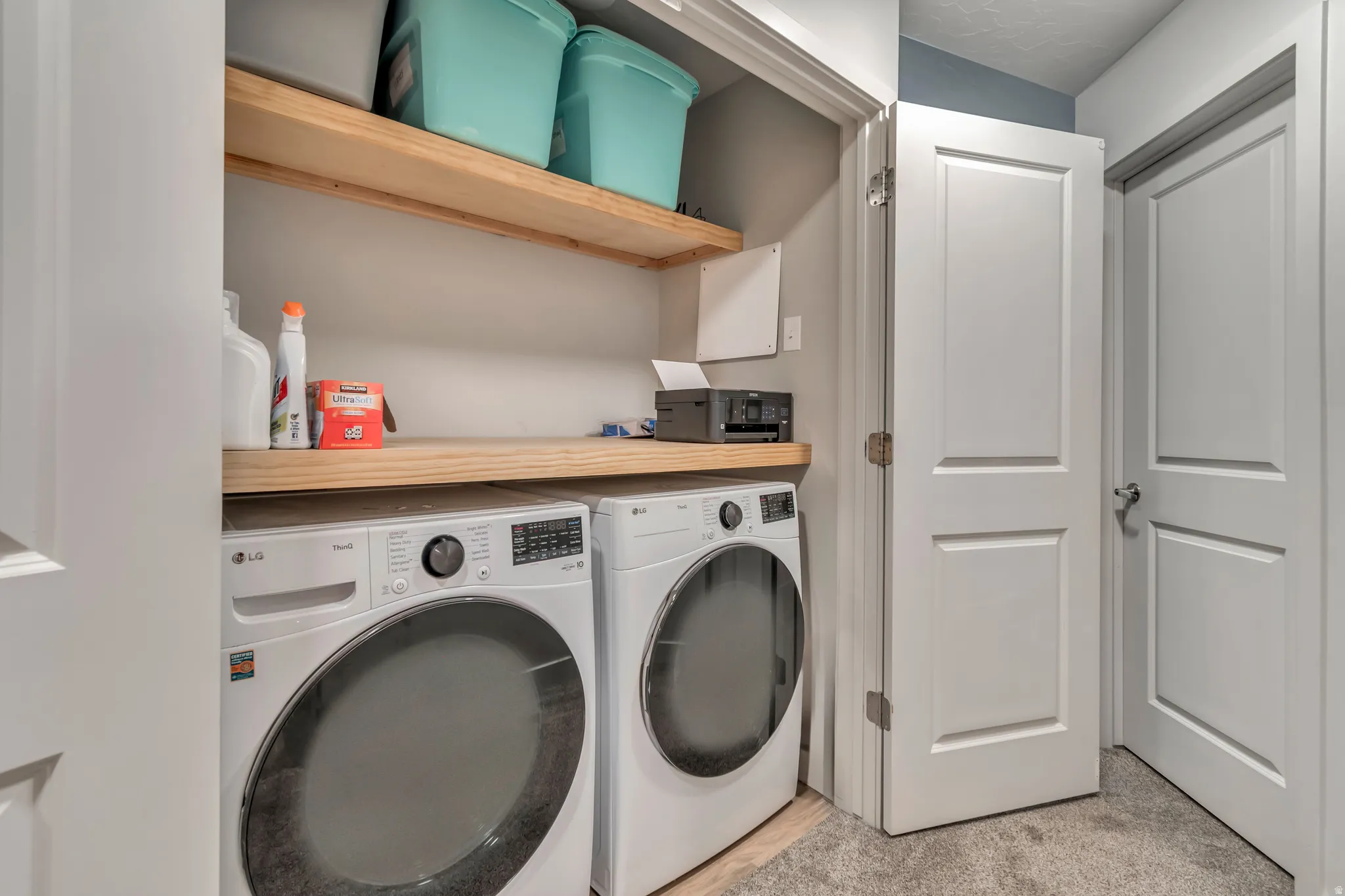 Dedicated laundry area featuring a washer and dryer, two light wood-finish shelves, and a coordinating wood-finish countertop