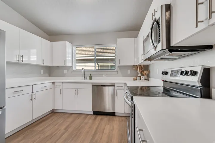 Kitchen featuring white cabinetry, light-toned countertops, stainless steel appliances, wood-finish flooring, and a window with blinds