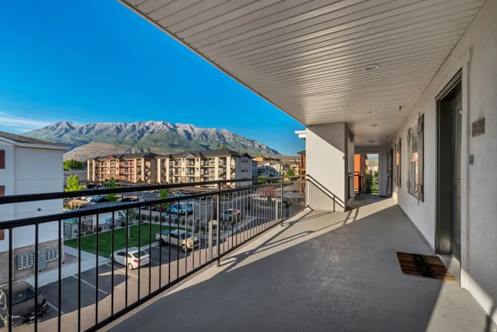 Outdoor balcony with black metal railing, overlooking a parking area, green space, and distant mountains