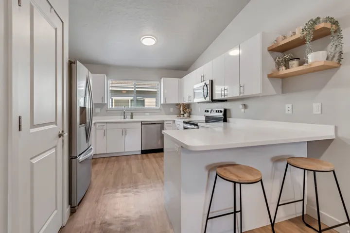 Kitchen featuring white cabinetry, stainless steel appliances, white countertops, wood-finish flooring, and open shelving