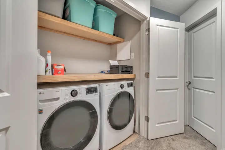 Dedicated laundry area featuring a washer and dryer, two light wood-finish shelves, and a coordinating wood-finish countertop